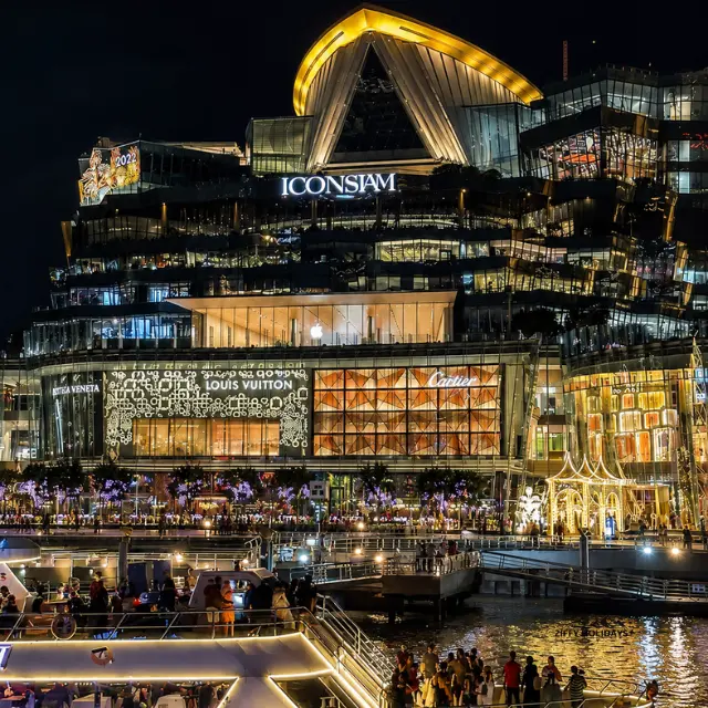 Illuminated exterior of ICONSIAM luxury shopping mall seen from the Chao Phraya River at night in Bangkok, Thailand.