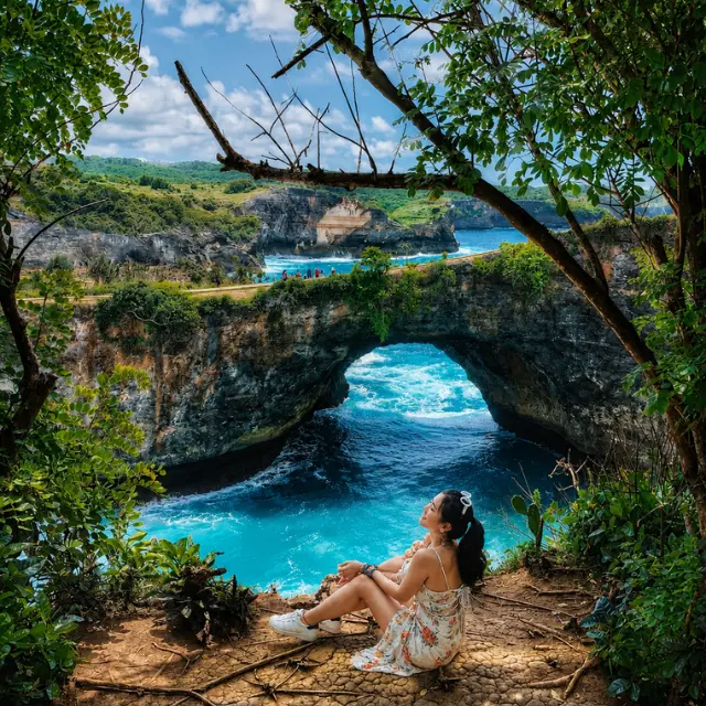 Couple enjoying the breathtaking view of Kelingking Beach in Nusa Penida, Bali from the famous cliff viewpoint.